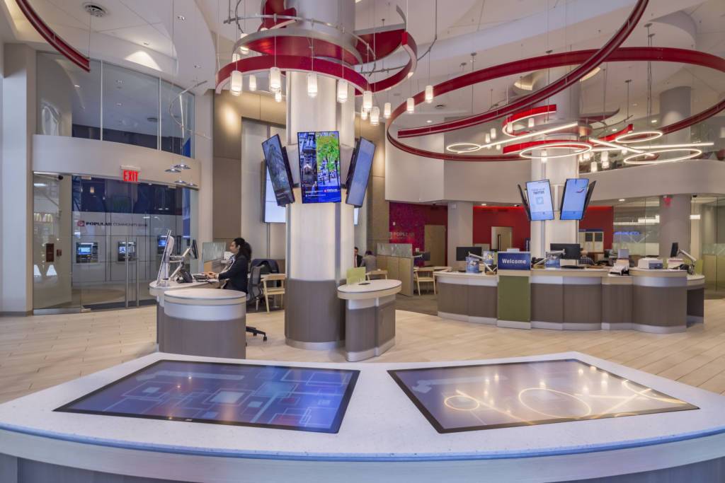 A bank lobby with multiple teller desks and many monitors hung on all the walls.