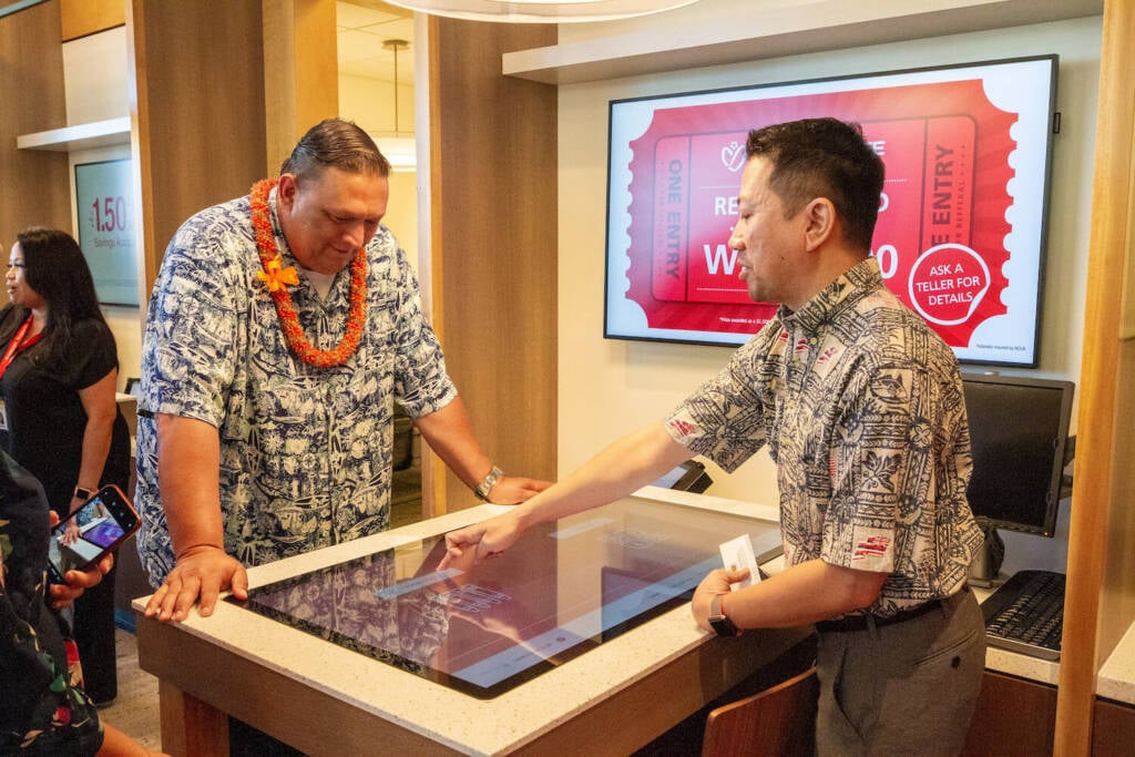 Bank-teller-talking-to-a-customer-over-an-electric-screen-desk.