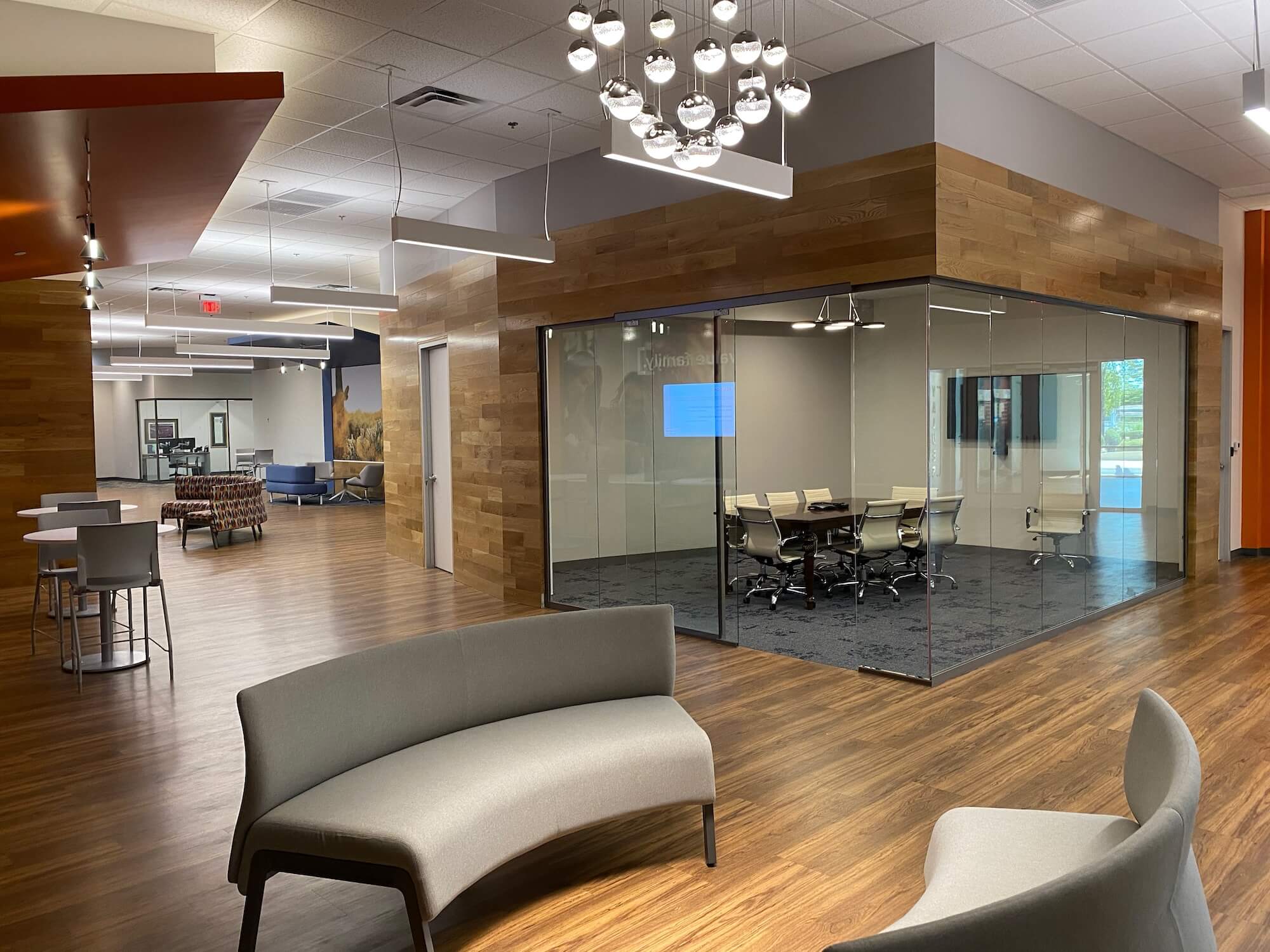 Modern bank interior featuring wood floors and walls, multi-functional spaces, a glass meeting room, and gray seating.