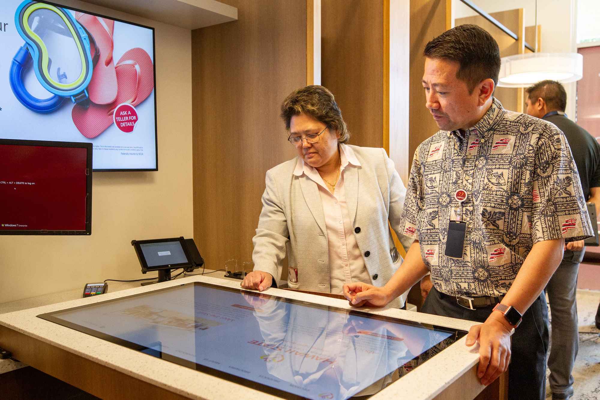 Two individuals engaged in discussion while examining a touch screen display in a modern room setting.